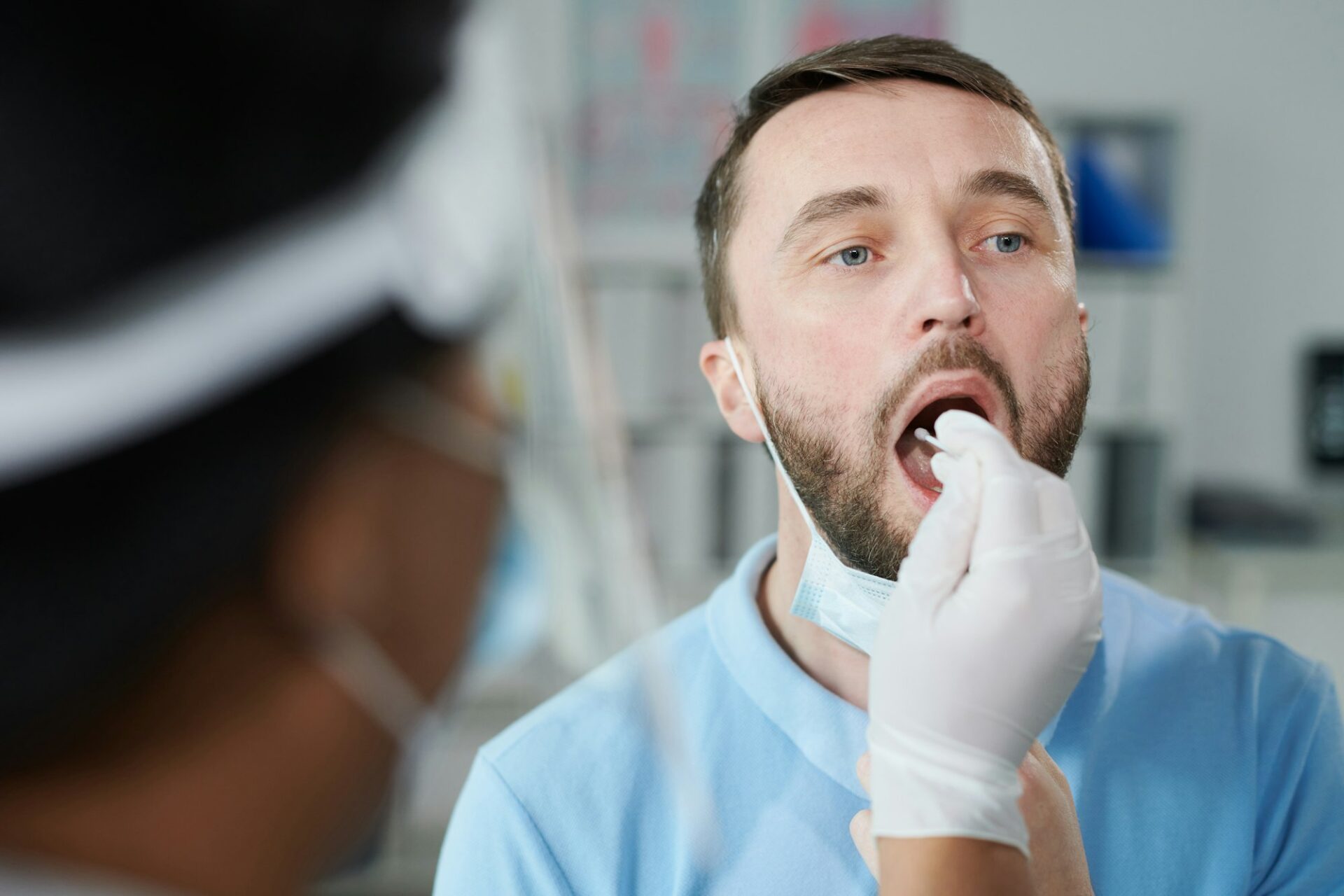 Face of young male patient being tested for covid with oral swab by gloved nurse
