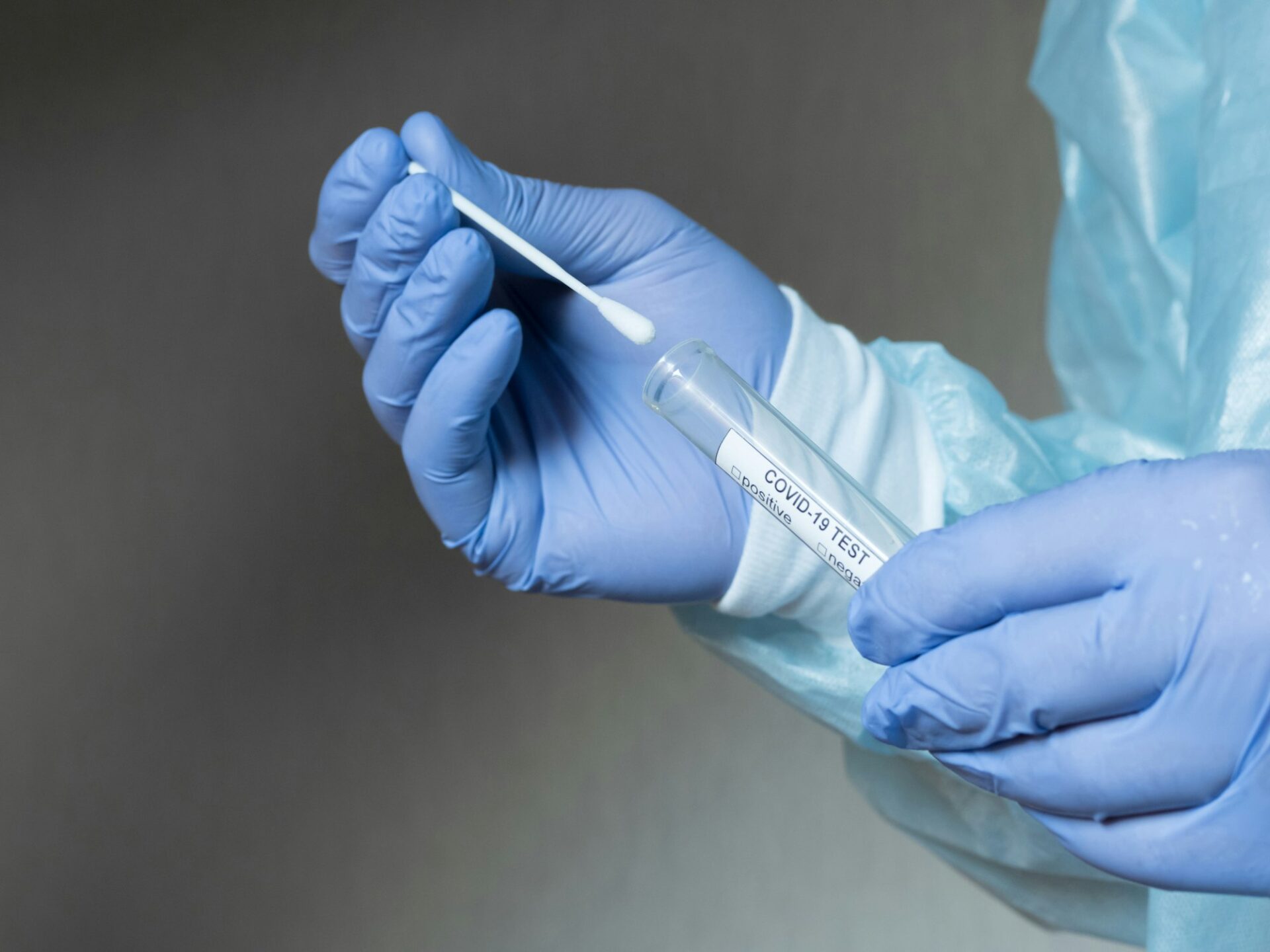 Hands in medical gloves holding an oral sample swab and a test tube for covid test