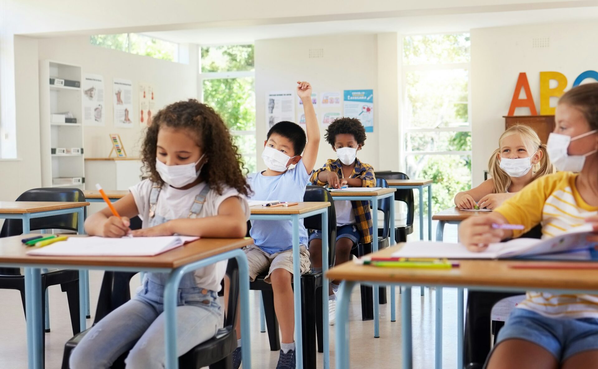 Young kids learning in classroom after covid pandemic, wearing protective face masks. Little childr